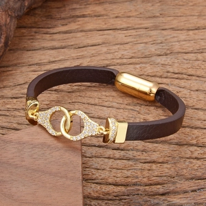Braunes Lederarmband mit goldenen Ringen und Pavé-Kristallen auf einem Holzuntergrund