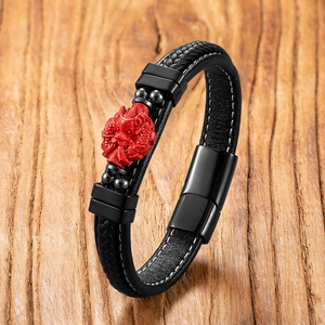 Detail of black woven leather bracelet with red dragon charm and magnetic clasp on wood