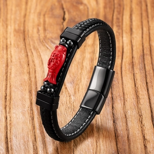Detailed view of woven black leather bracelet with red koi lucky charm on wood surface