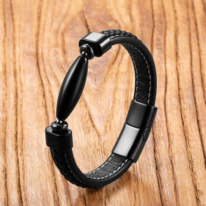 Detail of black woven leather men's bracelet with polished metal insert on wood background