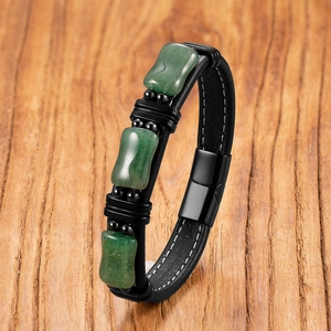 Men's black leather bracelet with green stone inlays and magnetic clasp on wood
