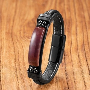 Macro detail of men's black braided leather bracelet with red-brown gemstone and metal clasp