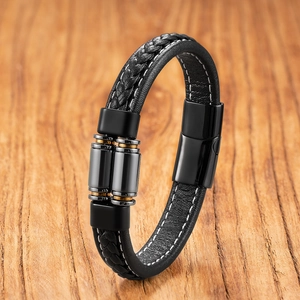 Dettaglio di bracciale in pelle intrecciata nera con cilindri oro e chiusura magnetica