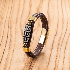 Detail of hand-woven brown leather bracelet with magnetic clasp and Dzi bead on wood