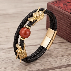 Detail of dragon-shaped golden charms with red agate bead on a braided leather bracelet