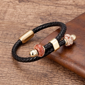 Detail van een zwarte gevlochten leren armband met gouden magneetsluiting en natuurstenen