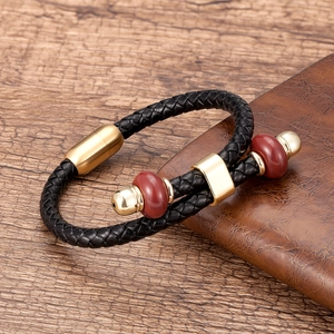 Detail van gevlochten zwart leren armband met gouden magneetsluiting en rode kralen