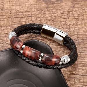 Gros plan sur un bracelet en cuir tressé noir avec trois pierres œil de tigre rouges