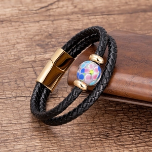 Dettaglio del bracciale in pelle intrecciata con perla in vetro floreale e chiusura oro