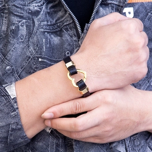 Modisches schwarzes Lederarmband mit ineinandergreifenden Goldherzen auf Denim