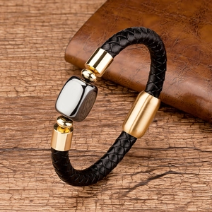 Close-up of woven black leather bracelet with gold clasp and grey square metal charm