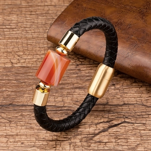 Close-up of woven black leather bracelet with gold metal hardware and orange agate stone