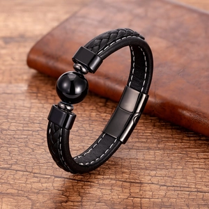 Détail d'un bracelet en cuir noir tressé avec perle polie posé sur une table en bois