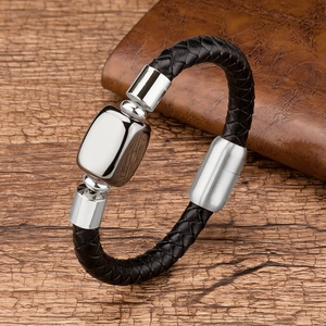 Close-up of black braided leather bracelet with silver metal charms on a dark wood table