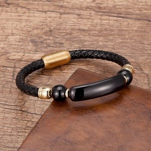 Close-up of men's black braided leather bracelet with golden magnetic clasp on leather desk