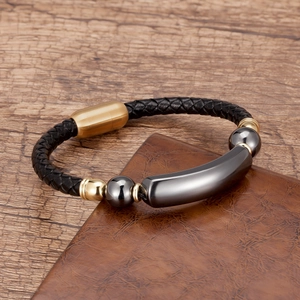 Braided black leather bracelet with gold magnetic clasp on a brown wooden background