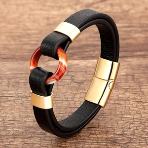 Close-up of woven leather bracelet with red agate bead and gold magnetic clasp on wood