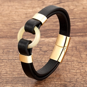 Detail of black braided leather bracelet with gold magnetic clasp and cream resin ring