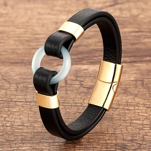 Close-up of black braided leather bracelet with gold magnetic clasp and green ring detail