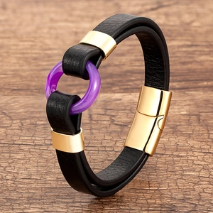 Detail of black braided leather bracelet with purple ring and gold magnetic clasp on wood