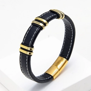 Detalle de una pulsera de cuero negro con anillos de metal dorado y costuras blancas