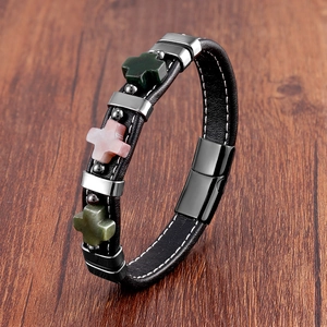Détail du bracelet en cuir avec breloques croix en métal et pierres sur bois