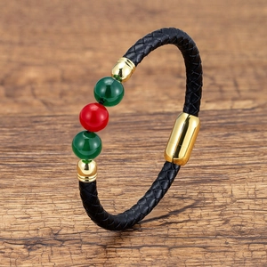 Detail of black braided leather bracelet with green and red beads and gold metal clasp