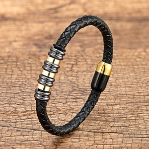 Dettaglio di bracciale in pelle intrecciata con anelli dorati e neri su fondo di legno