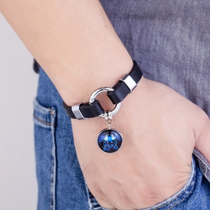 Detail of Gemini zodiac leather bracelet with blue pendant worn on person with denim jeans
