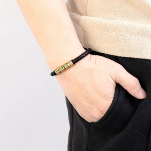 Bracciale in pelle nera intrecciata con cilindri in metallo dorato indossato da uomo