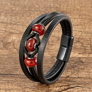 Détail d'un bracelet multicouche en cuir noir avec perles rouges et fermoir magnétique