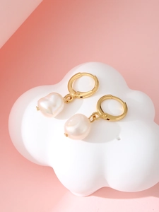 Detailed view of gold hoop earrings with irregular baroque pearls on a soft pink background