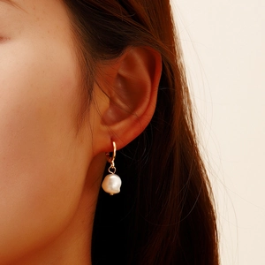 Detailed view of elegant baroque pearl earrings on a model with vintage gold hoop style