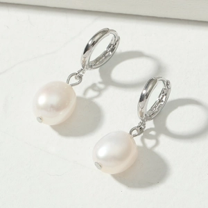 Elegant silver hoop earrings with white pearl pendants displayed on a textured grey base