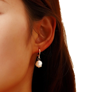 Elegant gold hoop earrings with natural baroque pearl pendant worn on model's ear