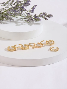 Set of 7 gold-colored geometric rings including flower and arrow designs on a display