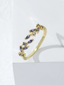 Detailed close-up of leaf-shaped ring with purple cubic zirconia on a minimalist white stand
