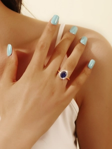 Macro view of princess-style oval blue gemstone ring with halo diamond setting on finger