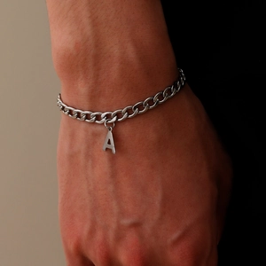 Detail van een zilveren Cubaanse schakelarmband met hanger letter A om de pols