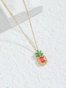 Detail of pineapple pendant with red oval stone and green marquise gems on gold chain