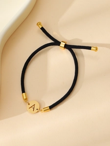 Détail du bracelet corde noire ajustable avec disque en métal doré gravé de la lettre A