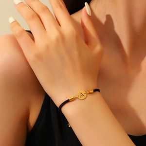 Gros plan d'un bracelet en corde tressée noire avec un pendentif lettre A doré poli