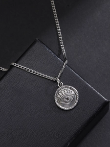 Macro detail of silver stainless steel evil eye pendant with textured edges on jewelry box