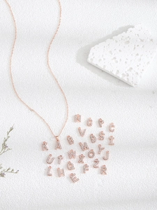 Detalle de colgantes de letras en oro rosa con cristales sobre una base de piedra blanca
