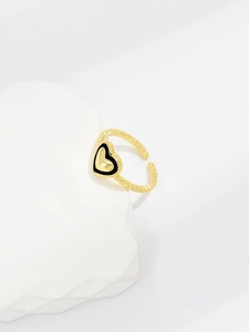 Detailed shot of golden heart ring with black enamel inlay on white textured background