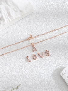 Detalle de colgantes de letras en oro rosa con cristales pavé sobre fondo blanco