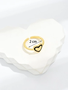 Close-up of golden adjustable heart ring with black enamel on a stone display