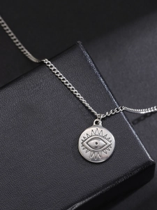 Detail of silver evil eye pendant on a chain over a black textured jewelry box