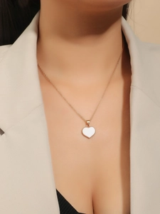 Detailed view of a gold heart pendant with white enamel inlay on a delicate chain