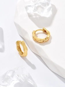 Macro detail of gold-plated bamboo texture hoop earrings on a white stone display